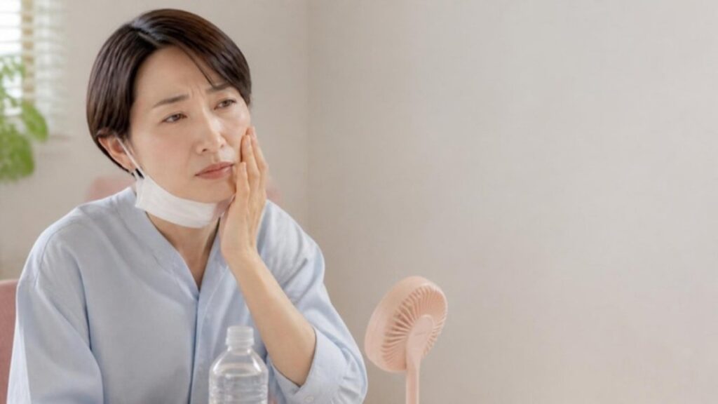 マスクをあごまで下げ、指先で頬に触れて肌の具合を確かめている50代の女性の画像