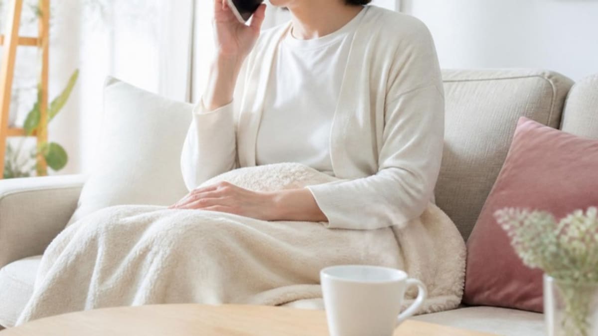 体調がつらい日に、自宅のソファでサロンに日程変更の電話をしている画像