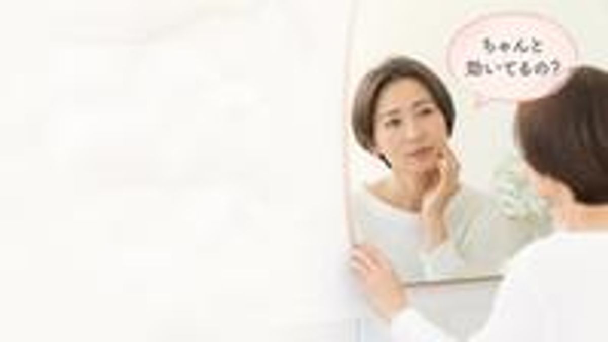 鏡の前で頬に触れて施術の効き目を確かめている女性のイラスト画像