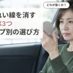 停車中の車の運転席で手鏡を目の高さに持って口もとをのぞき込み、ほうれい線を消す方法のどれが自分に届くのか迷っている女性の画像